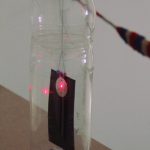 Pop-bottle magnetometer close in showing bottle with pebbles, card and sequin lit by laser.
